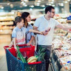 Happy family with child and shopping cart buying food at grocery store or supermarket